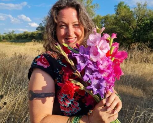 Iris lächelt mit einem Strauß Gladiolen in die Kamera