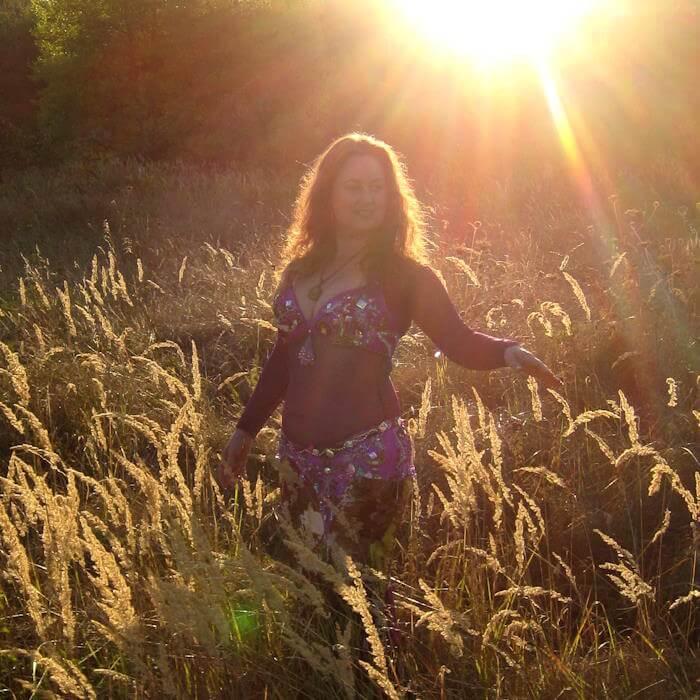 Iris tanzt in der Wiese mit hohen goldenen Grashalmen, die Sonne geht langsam unter und die goldenen Strahlen beleuchten die Szene