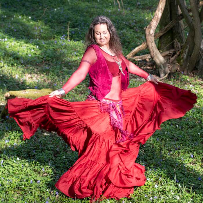 Iris tanzt lächelnd im roten Kleid im Wald mit blühendem Bodendeckern
