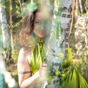 Iris lachend mit grünen Kleid zwischen Birkenstämmen im Wald