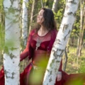 Iris lachend mit rotem Kleid zwischen Birkenstämmen im Wald