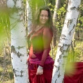 Iris lachend mit rotem Kleid zwischen Birkenstämmen im Wald