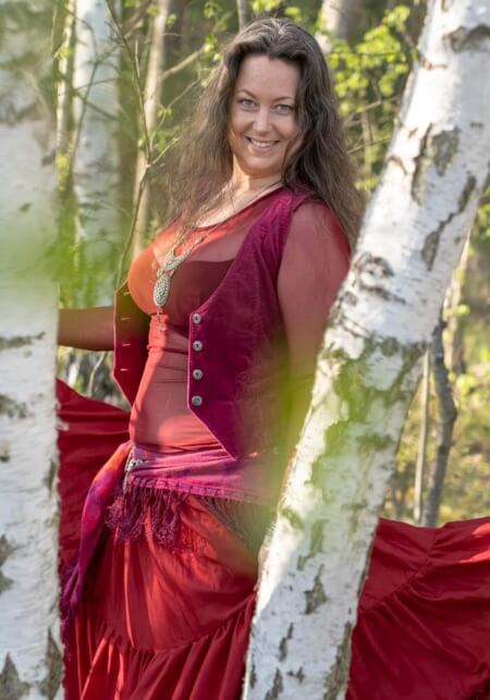 Iris lachend mit rotem Kleid zwischen Birkenstämmen im Wald