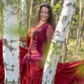 Iris lachend mit rotem Kleid zwischen Birkenstämmen im Wald