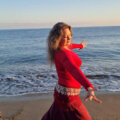Iris tanzt in roter Kleidung am Strand