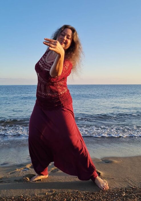 Iris tanzt in roter Kleidung am Strand