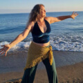 Iris tanzt in petrol-gold farbener Kleidung am Strand