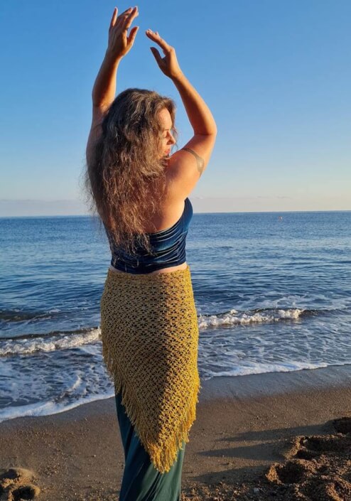 Iris tanzt in petrol-gold farbener Kleidung am Strand