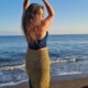 Iris tanzt in petrol-gold farbener Kleidung am Strand