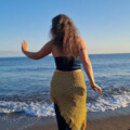 Iris tanzt in petrol-gold farbener Kleidung am Strand