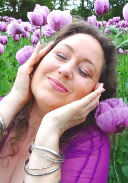 Iris lächelt mit geschlossenen Augen in einem Meer von pinken Mohnblumen